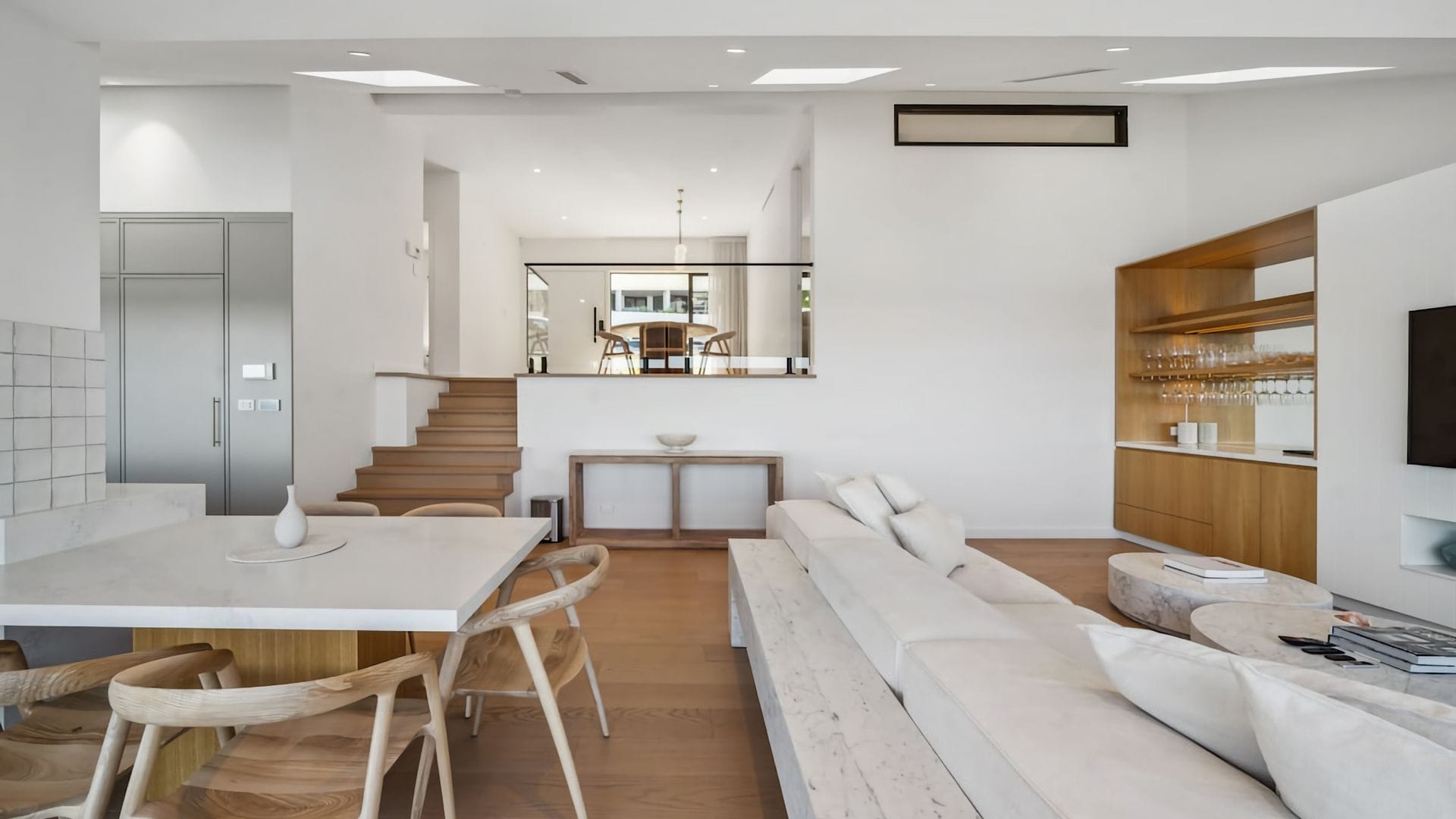 A modern kitchen with a dining area, a staircase leading to a dining room, and a living area with a sofa and a TV.
