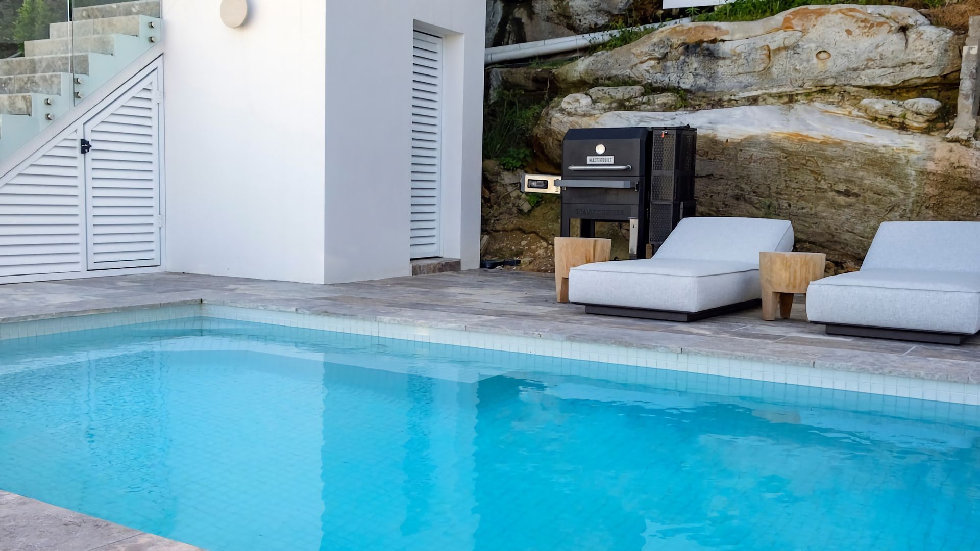 A swimming pool with two lounge chairs and a barbecue grill.