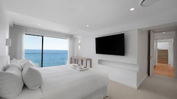 A modern hotel room with a large bed, a TV mounted on the wall, and a view of the sea through a large window.