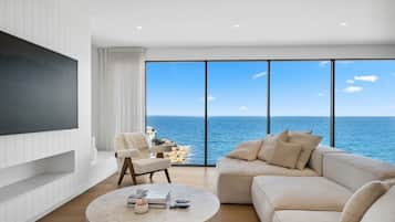 A modern living room with a large TV, a sofa, a coffee table, and a view of the ocean.