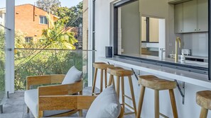 A balcony with a seating area, a window overlooking a building, and a kitchen area with modern appliances.