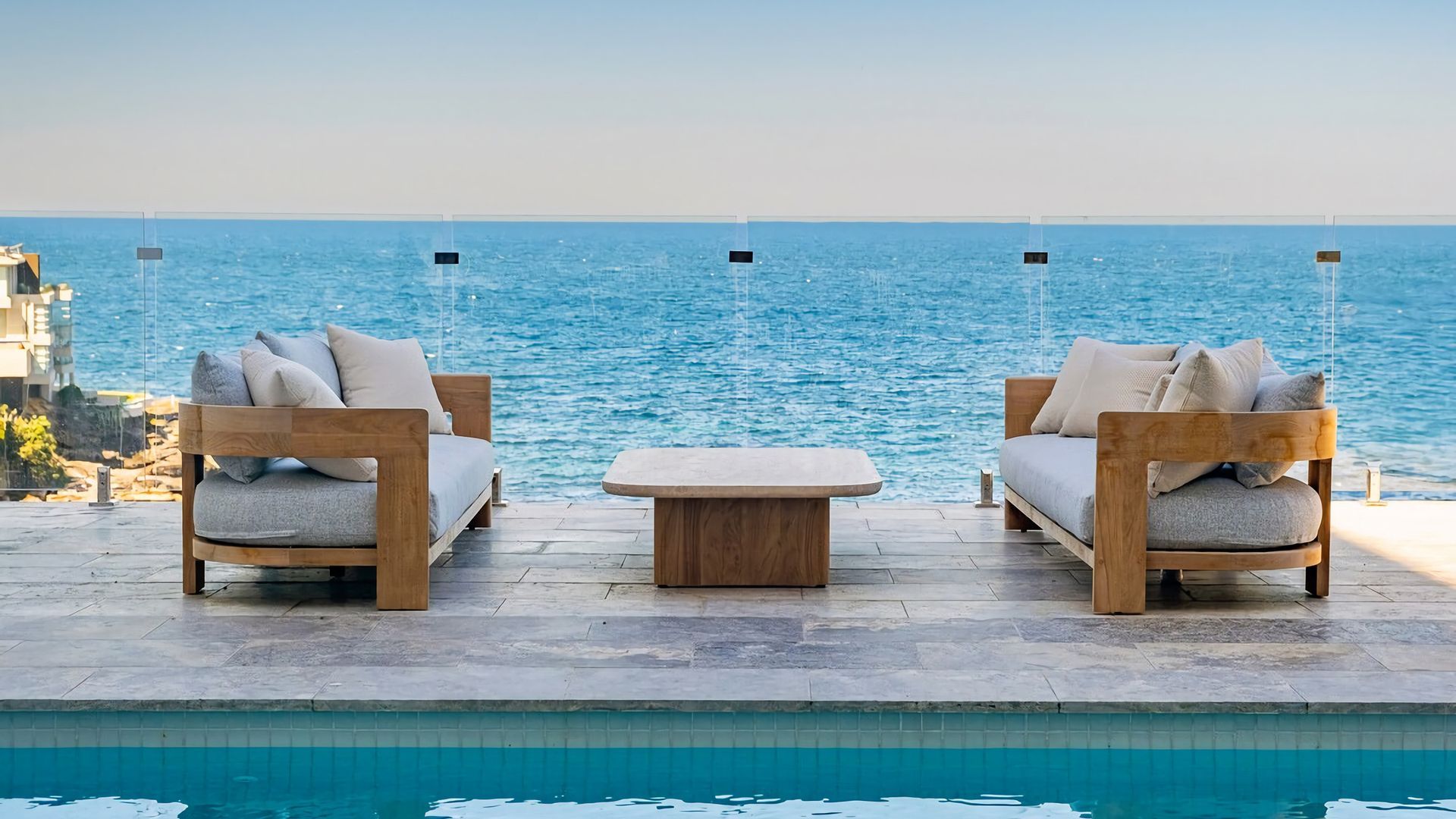 A poolside seating area with two sofas and a small table, overlooking a body of water.
