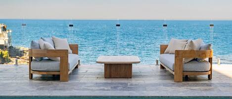 A poolside seating area with two sofas and a small table, overlooking a body of water.