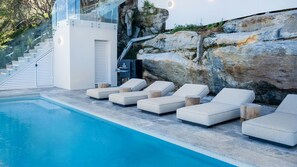 A poolside area with lounge chairs, a staircase, and a rock formation. - South Coogee Escape, Heated Pool & Spacious Living (Maroubra)