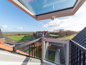 A residential building with a large skylight, a view of a green field, and a distant body of water. - Luxe villa with sauna, hottub and garden (Colijnsplaat)
