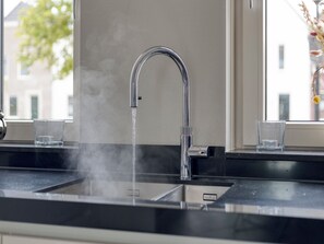Een moderne keuken met een roestvrijstalen kraan, twee glazen op het aanrecht en een raam met uitzicht op gebouwen en bomen.