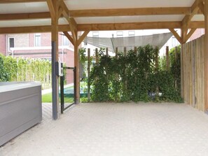 A covered outdoor area with a sandy floor, wooden beams, a metal gate, and a hedge. - Luxe villa with sauna, hottub and garden (Colijnsplaat)