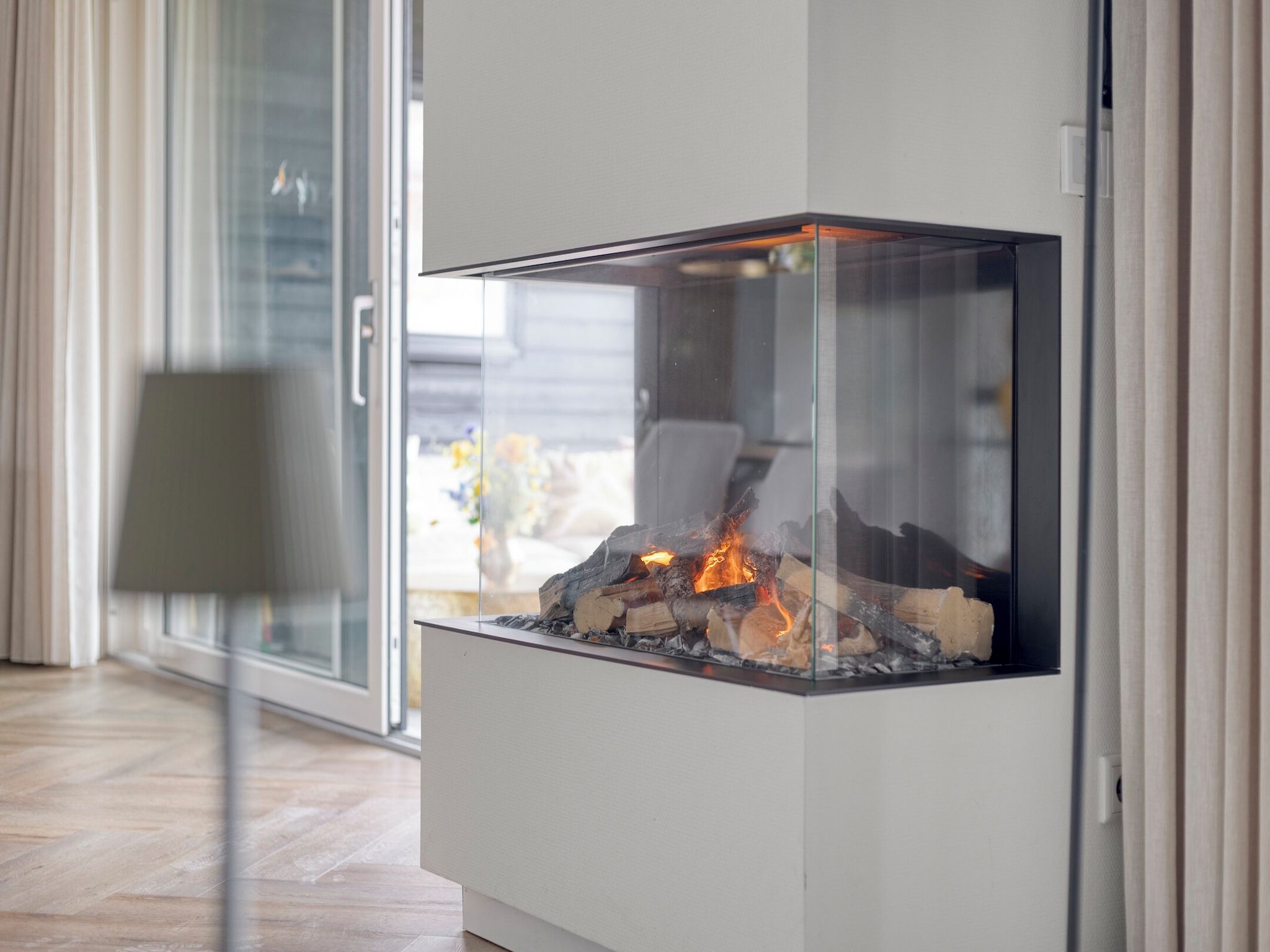 Ein moderner Kamin mit Glaseinschluss in einem Raum, der durch eine Schiebetür mit einem Außenbereich verbunden ist.