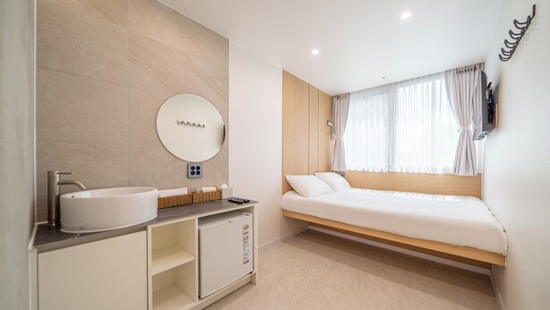 Un dormitorio moderno con una cama, armario empotrado, espejo redondo y baño con lavamanos y refrigerador.