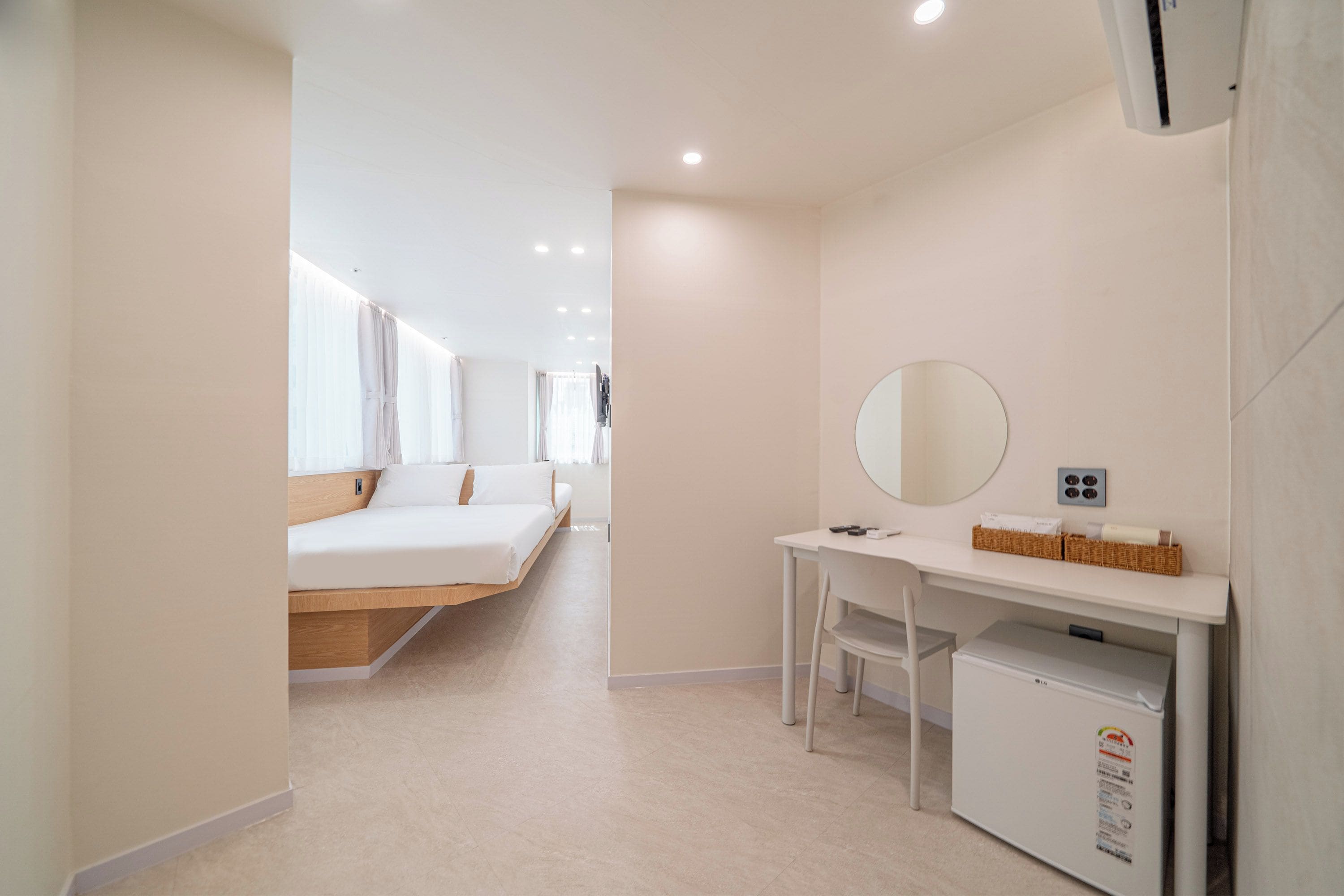 Une chambre d’hôtel moderne équipée d’un lit, d’un bureau, d’un miroir et d’un petit réfrigérateur.