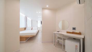 Une chambre d’hôtel moderne équipée d’un lit, d’un bureau, d’un miroir et d’un petit réfrigérateur.