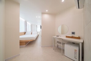 Una habitación de hotel moderna con una cama, un escritorio, un espejo y un refrigerador pequeño.