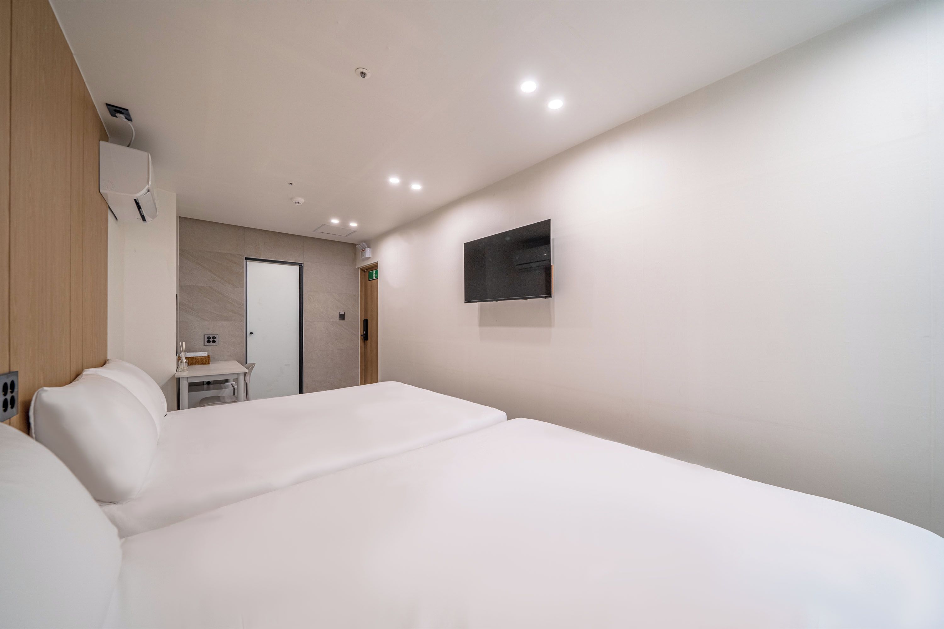 A hotel room with a large bed, a small table, a mirror, and a TV on the wall.