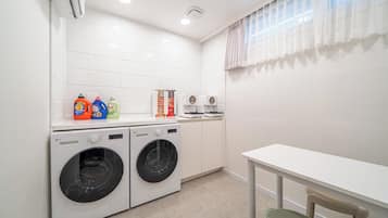 A laundry room with two front-loading washing machines, a table, and a chair.
