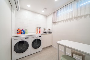 A laundry room with two front-loading washing machines, a table, and a chair. - Melo Stay Seoul (Seoul)