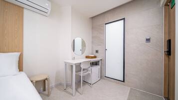 Quarto de hotel moderno com uma cama, escrivaninha, espelho, armário pequeno e porta.
