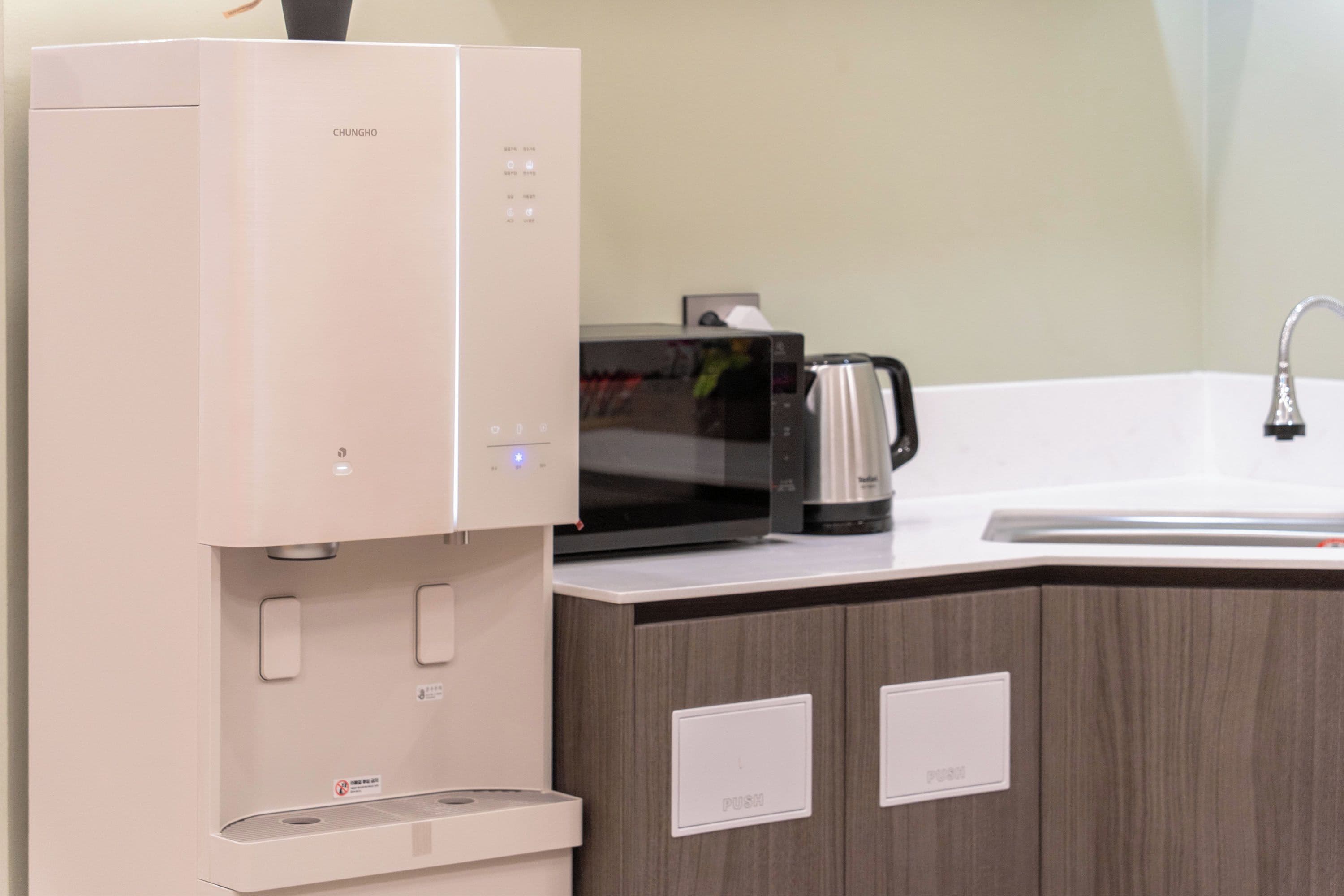 A kitchen with a built-in microwave, a kettle, and a sink.