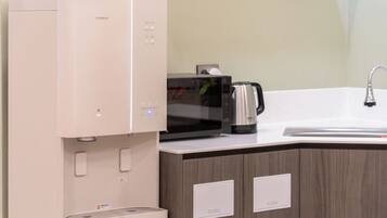 A kitchen with a built-in microwave, a kettle, and a sink.