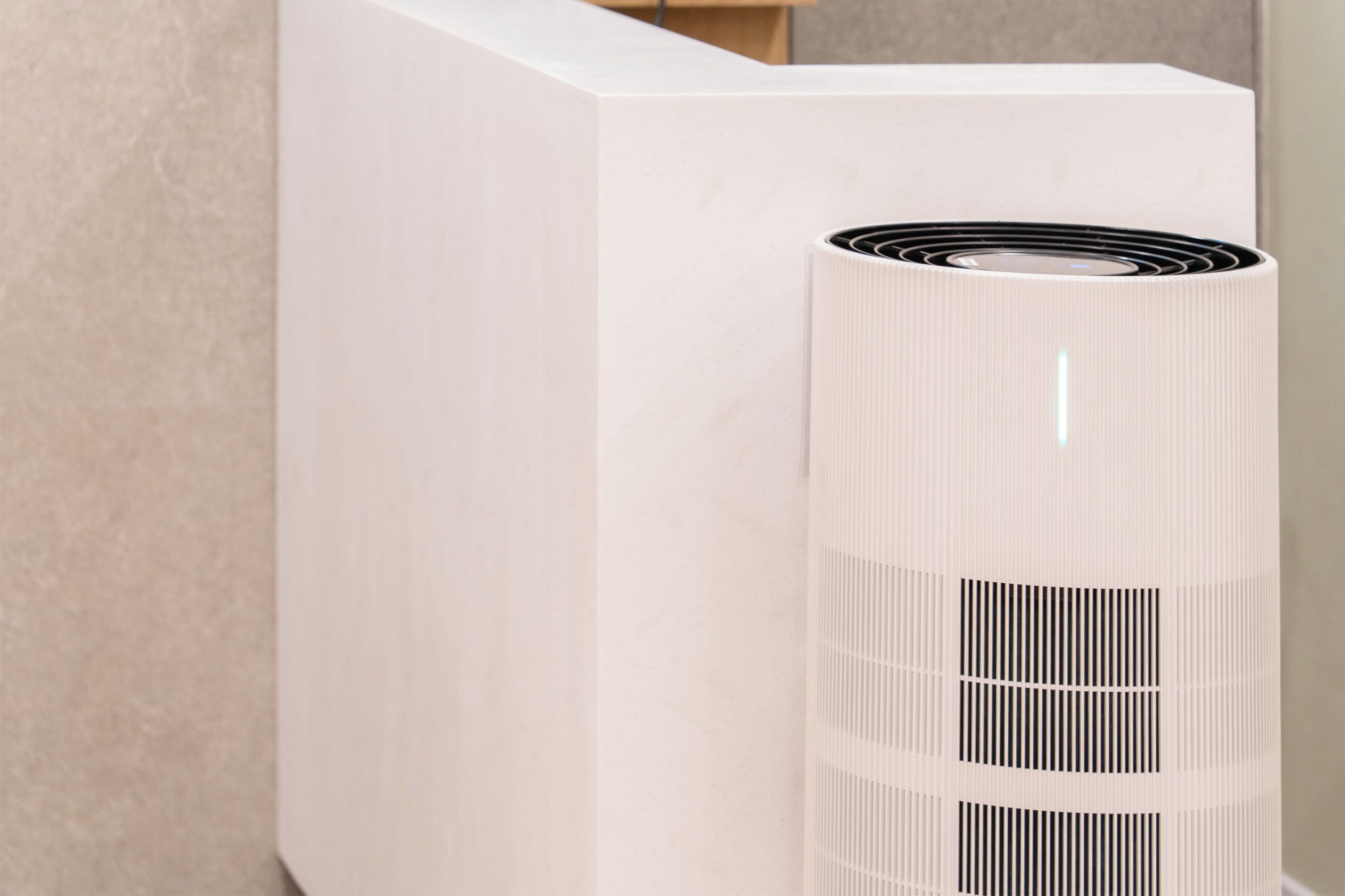 A white cylindrical air purifier with a ribbed design, placed against a wall.