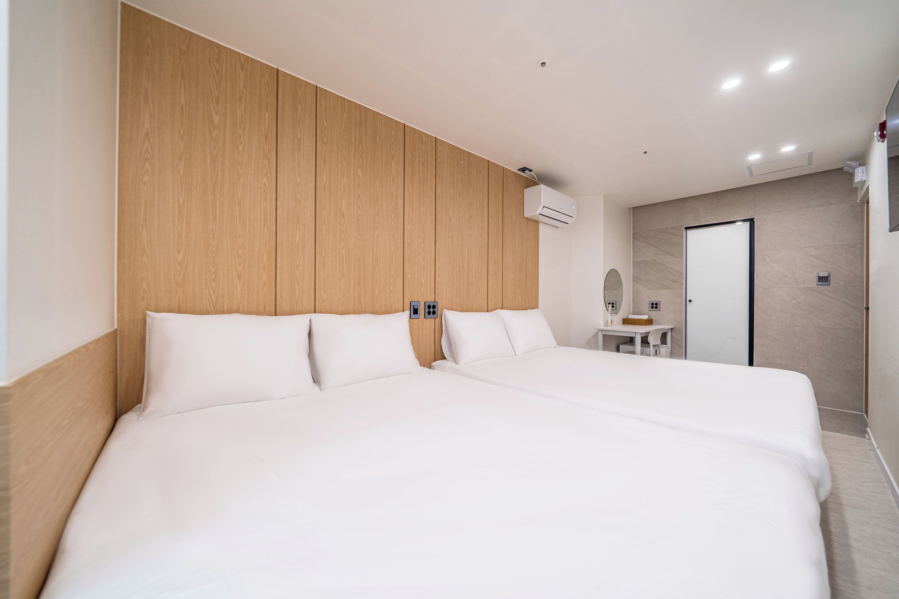 Habitación de hotel con una cama grande, cabecera de madera, mesitas de noche, un espejo y un baño con ducha.