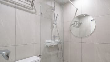 Un baño moderno con ducha envuelta en vidrio, inodoro y espejo redondo.