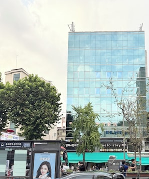 A modern building with a glass facade, surrounded by trees and a street with vehicles and pedestrians. - Melo Stay Seoul (Seoul)