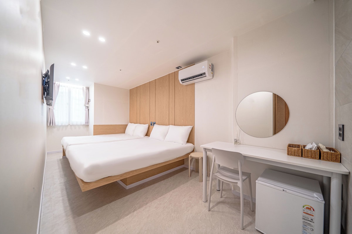 A hotel room with a bed, desk, chair, air conditioning unit, and a refrigerator.