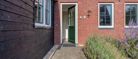 A brick house with a wooden exterior, a green door, and a small garden with purple flowers.