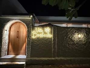 A villa entrance with a wooden door and a neon sign reading 'Villa Basheera.' - Villa Basheera (Gili Trawangan)