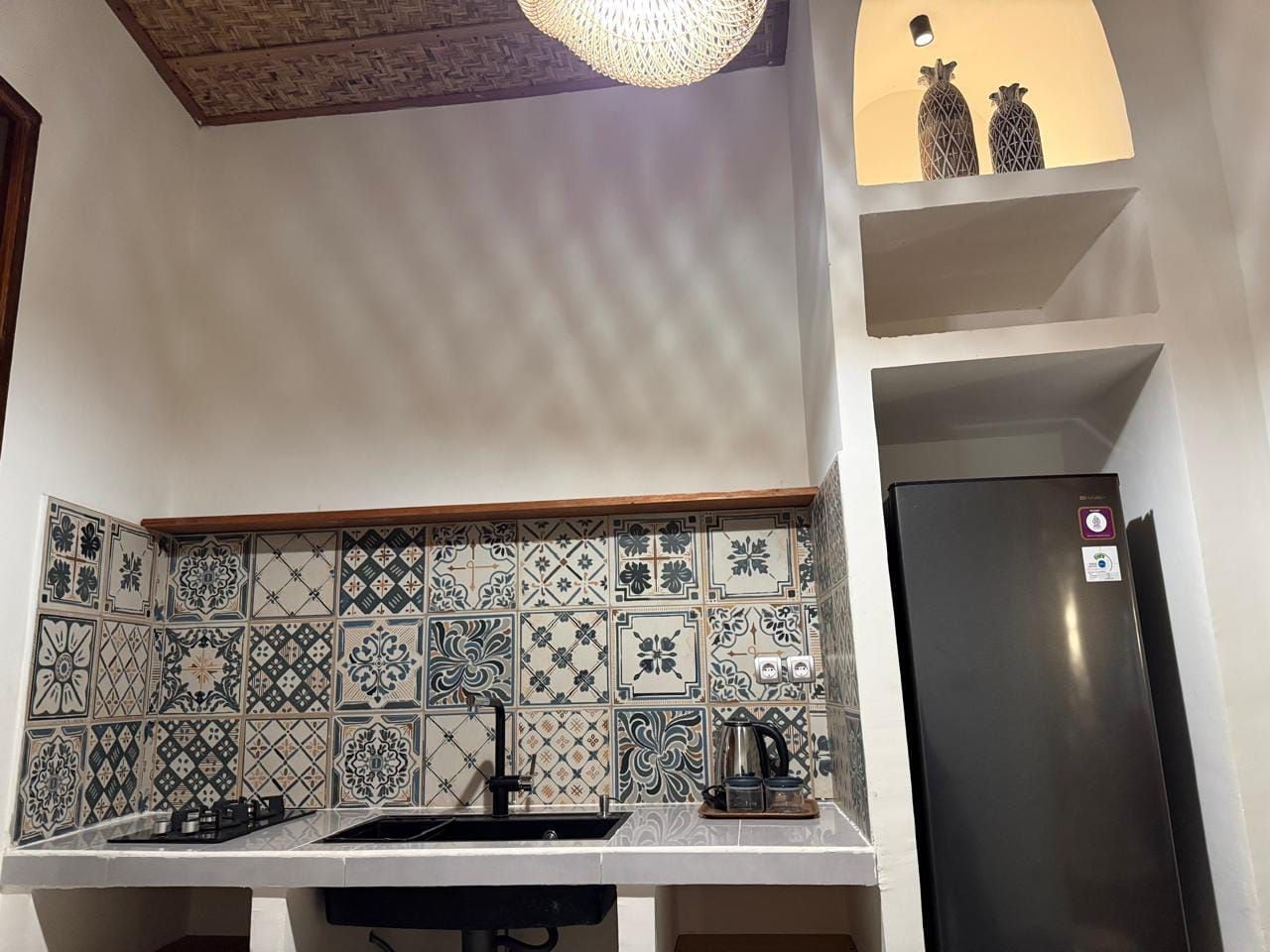 Una cocina con baldosas estampadas, un refrigerador negro y una lámpara colgante.