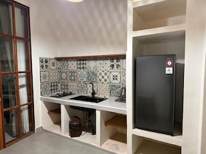 Eine Küche mit gefliestem Rücksprüher, einem schwarzen Kühlschrank und einem Spülbecken mit Wasserhahn.