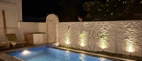 Una piscina con pared texturizada y pequeñas plantas, rodeada de piso de ladrillo.