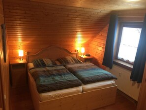 Ein Zimmer mit Holzwänden, einem Bett, zwei Nachttischlampen und einem mit Vorhängen versehenen Fenster.