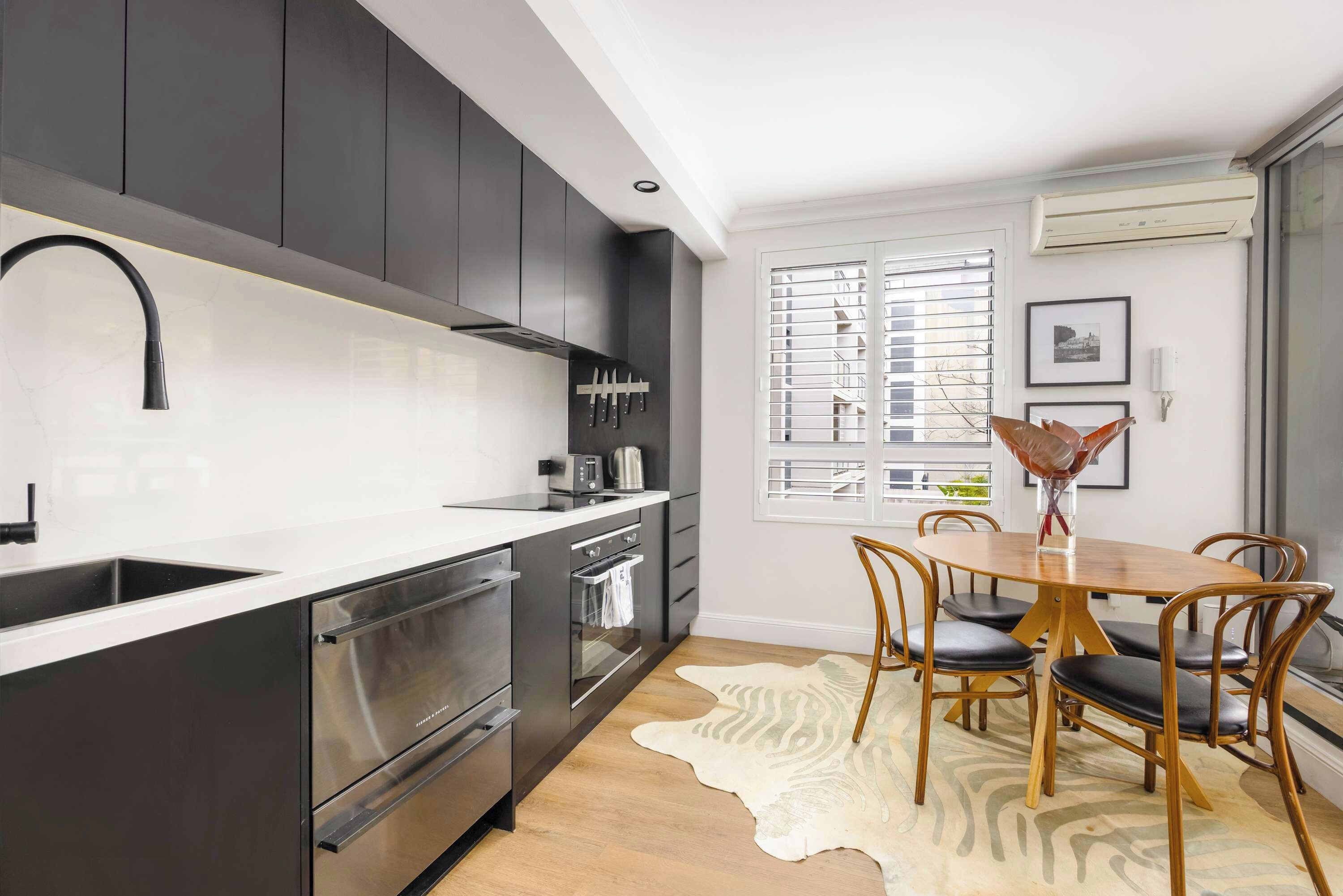 A modern kitchen with dark cabinets, stainless steel appliances, and a dining area with a wooden table and chairs.