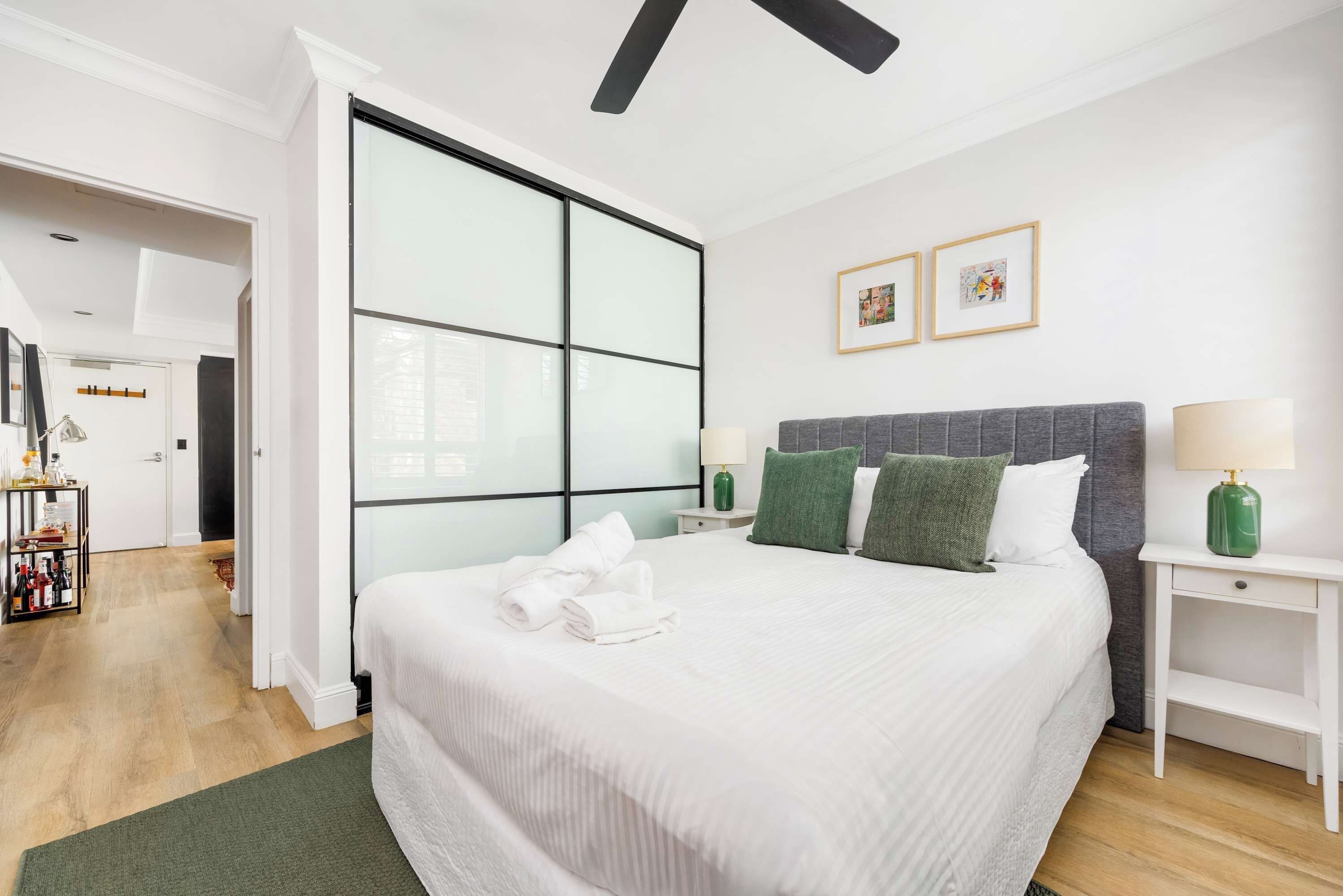 Ein Hotelzimmer mit einem großen Bett, einem Nachttisch, einem Beistelltisch, einem grünen Teppich und einer Wand mit zwei gerahmten Bildern.