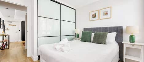 Une chambre d’hôtel avec un grand lit, une table de chevet, une commode, un tapis vert et un mur orné de deux tableaux encadrés.