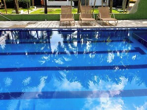 Una piscina con agua cristalina, rodeada de sillones de descanso y un césped cuidado.