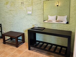 Una habitación con una pared verde texturizada, una mesa de madera con una bandeja, un taburete pequeño y una cama con almohadas.