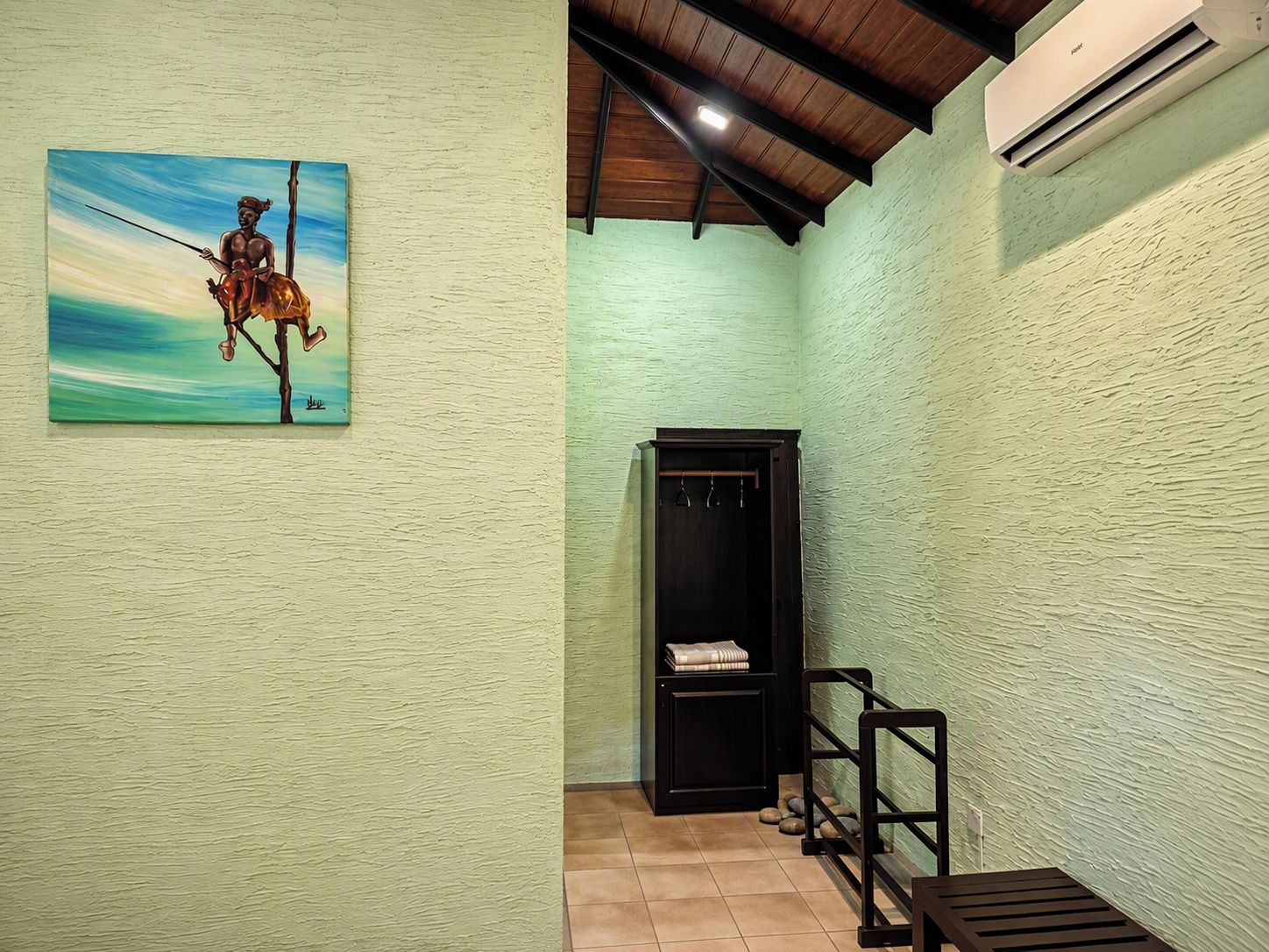 Una habitació amb una paret verda amb textura, un quadre amb una figura a cavall, una porta de fusta i un aparell d'aire condicionat.