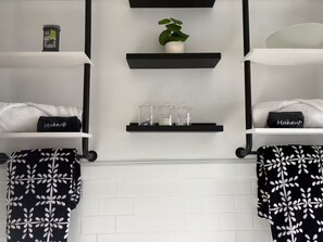 A bathroom with a white tiled wall, black towel racks, and shelves holding a plant, a container, and toiletry items. - King Bed in Oak Park w/Chicago Chic (Oak Park)