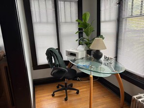 A modern office space with a glass table, a black office chair, a potted plant, and a lamp. - King Bed in Oak Park w/Chicago Chic (Oak Park)