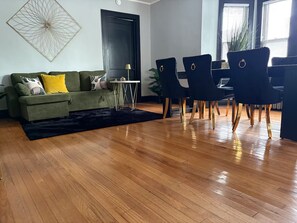 A modern living room with a green sofa, a black rug, and a dining area with black chairs and a white table. - King Bed in Oak Park w/Chicago Chic (Oak Park)