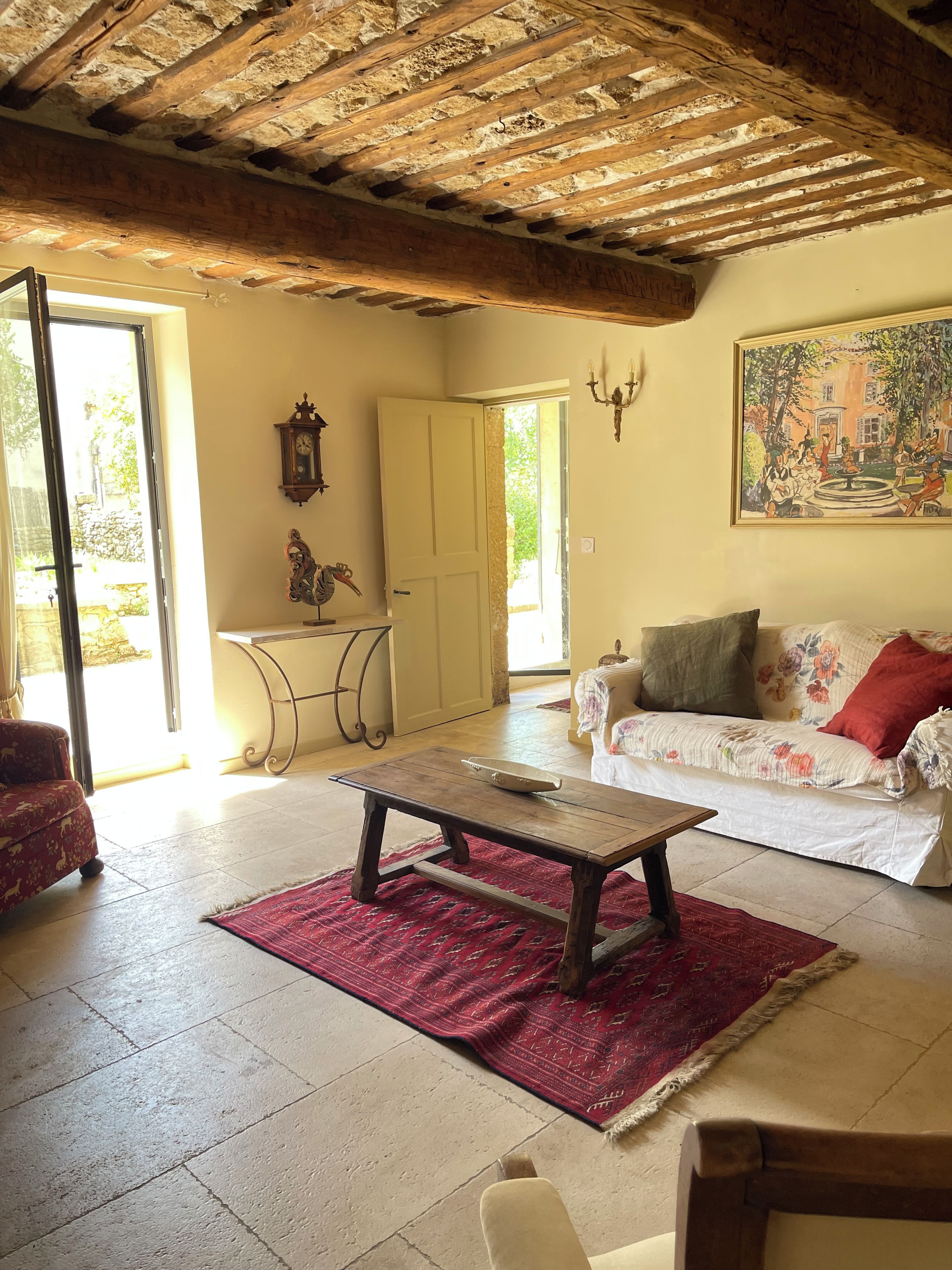 A room with a wooden ceiling, a sofa with floral upholstery, a red rug, and a painting on the wall.