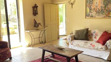 A room with a wooden ceiling, a sofa with floral upholstery, a red rug, and a painting on the wall.