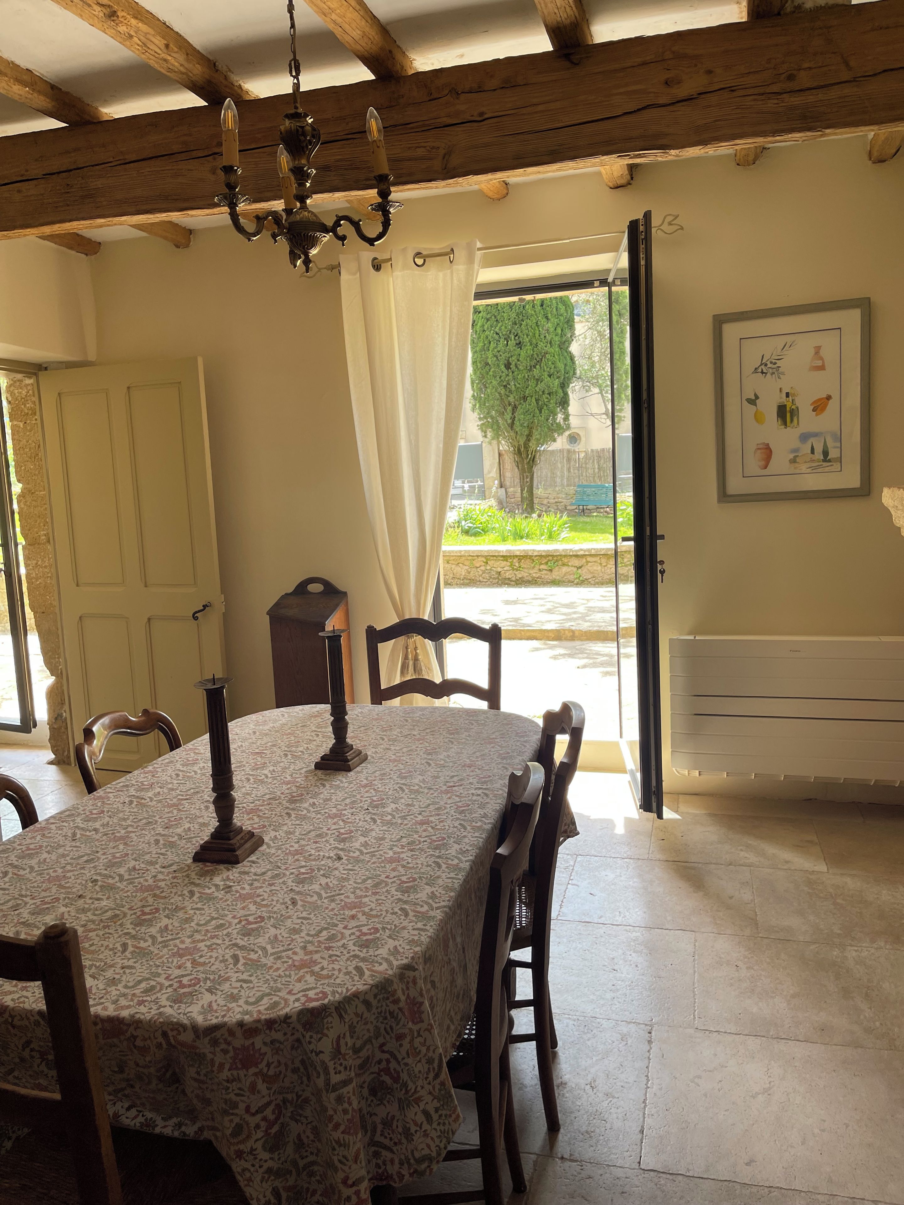 A dining area with a round table, chairs, a chandelier, and a view of the outdoors.