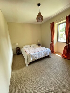 Un dormitorio con una cama, dos lámparas de noche, un candelabro colgante y una ventana con cortinas.