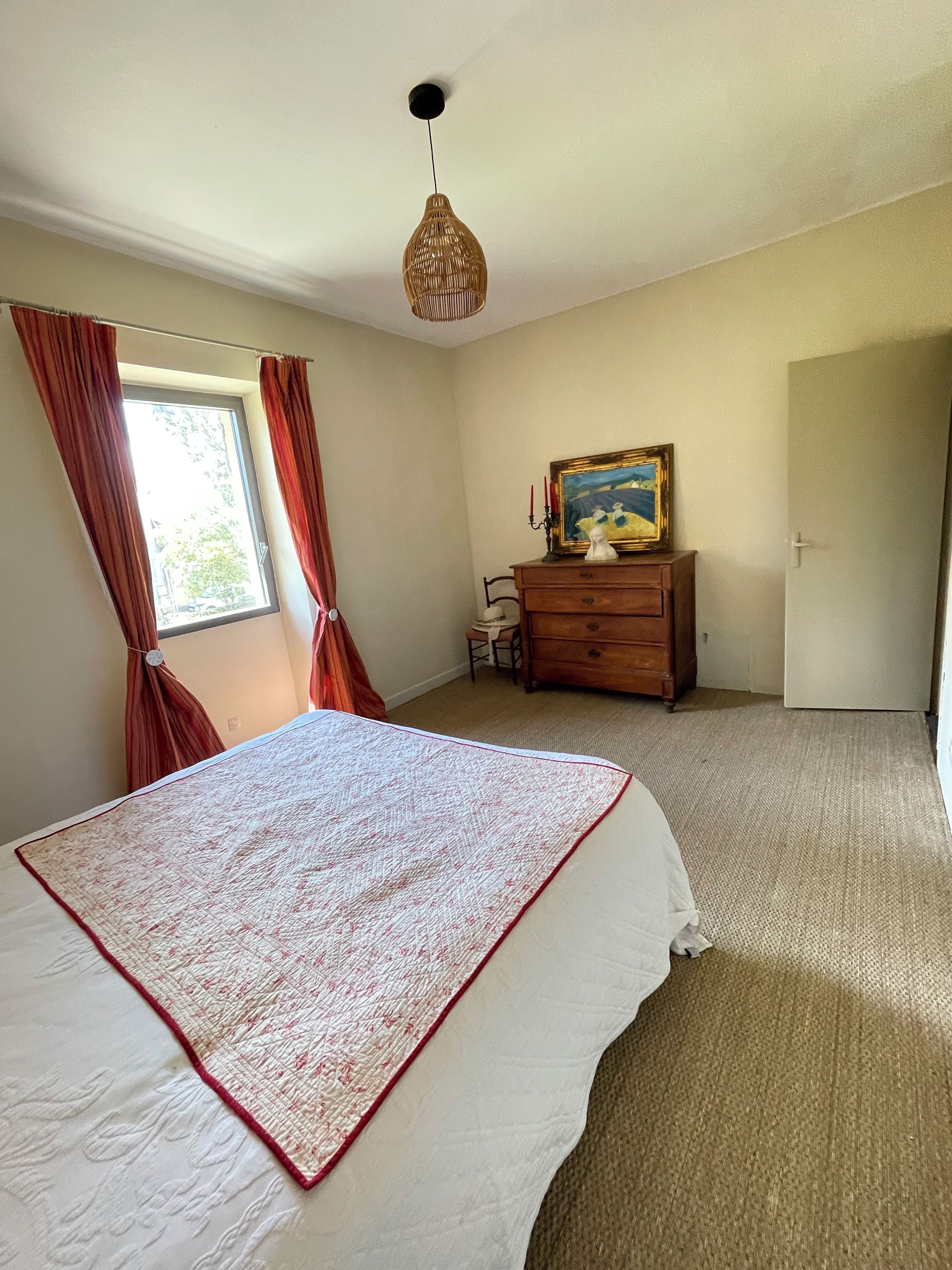 Une chambre à coucher avec un lit, une commode, un tableau et une fenêtre avec des rideaux.