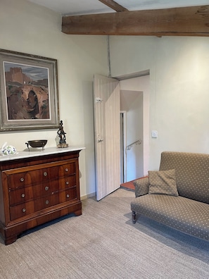 Una habitación con un aparador de madera, un cuadro, un sofá y una puerta que da a otra estancia.