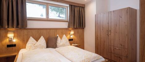 Une chambre à coucher avec un lit, une tête de lit en bois, deux lampes de chevet, une armoire et une fenêtre avec des rideaux.