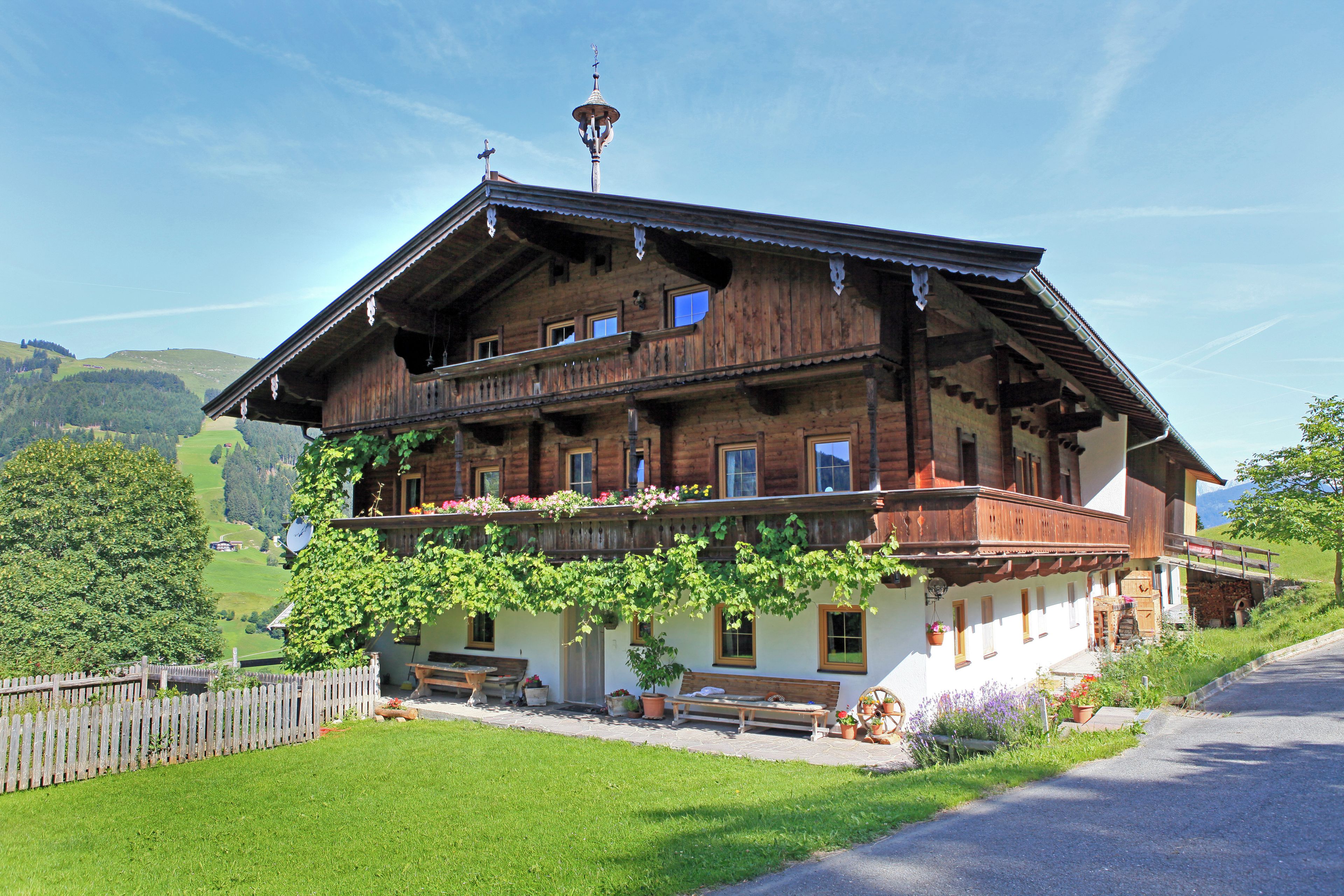 A traditional wooden chalet with a balcony, a small garden, and a view of the surrounding hills.